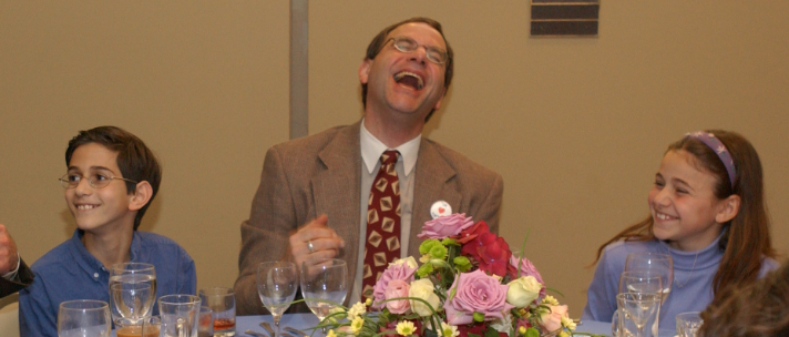 Man laughing joyfully at a formal event with flowers.