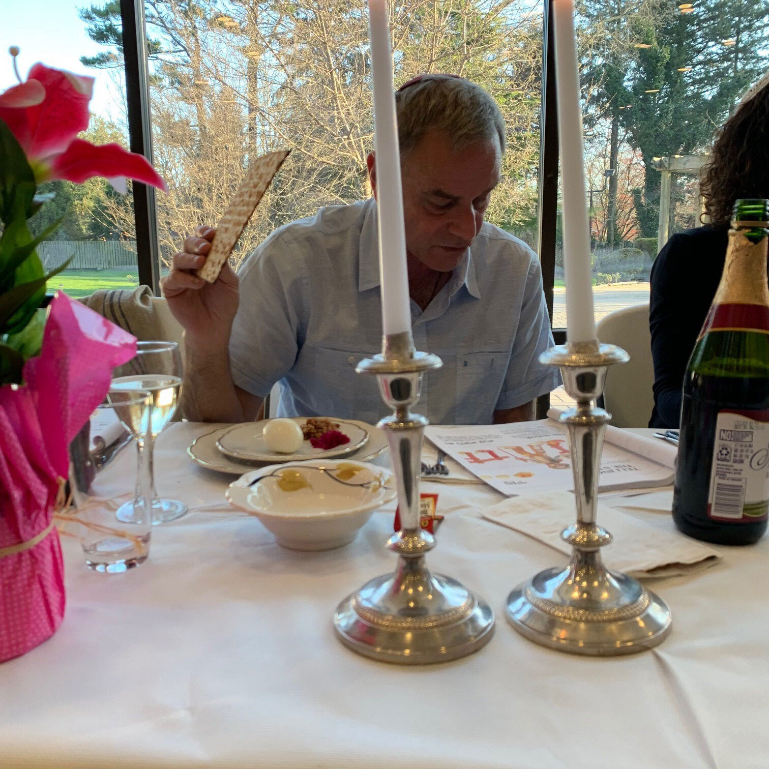 Man enjoying a meal at a candlelit table with flowers and wine.