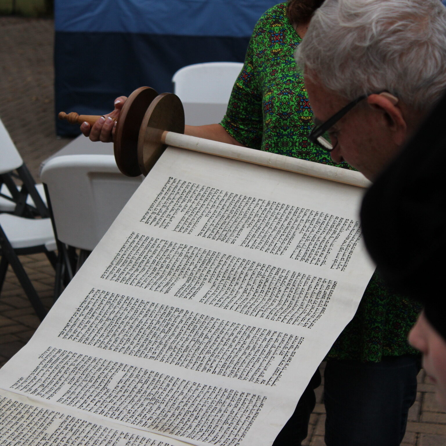 Person reading an ancient scroll with Hebrew text outdoors.