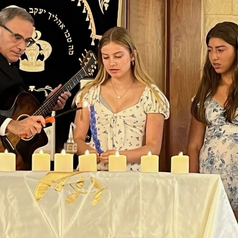 A man in religious attire leads a ceremony with three girls at a table with candles.