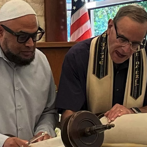 Two men examining a Torah scroll in a synagogue setting.