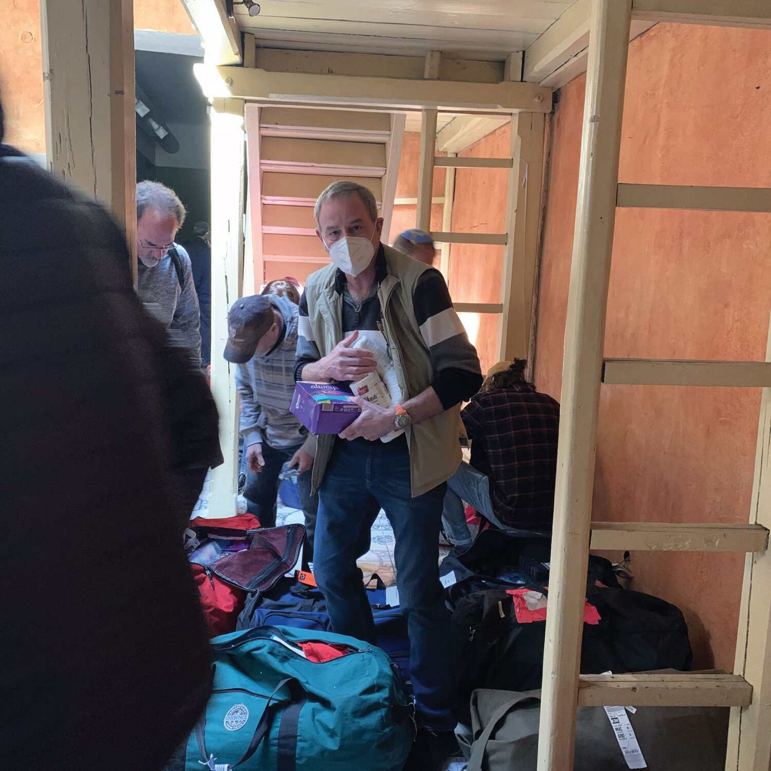 People with luggage inside a narrow indoor space, some wearing masks.