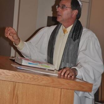 Man speaking at a podium wearing a white robe and scarf.
