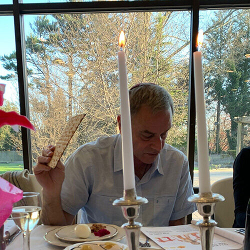 Man sitting at a table with candles and food, holding a knife and fork.