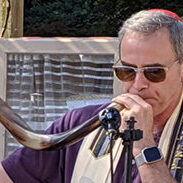 Man reading from a book with a prayer shawl outdoors.